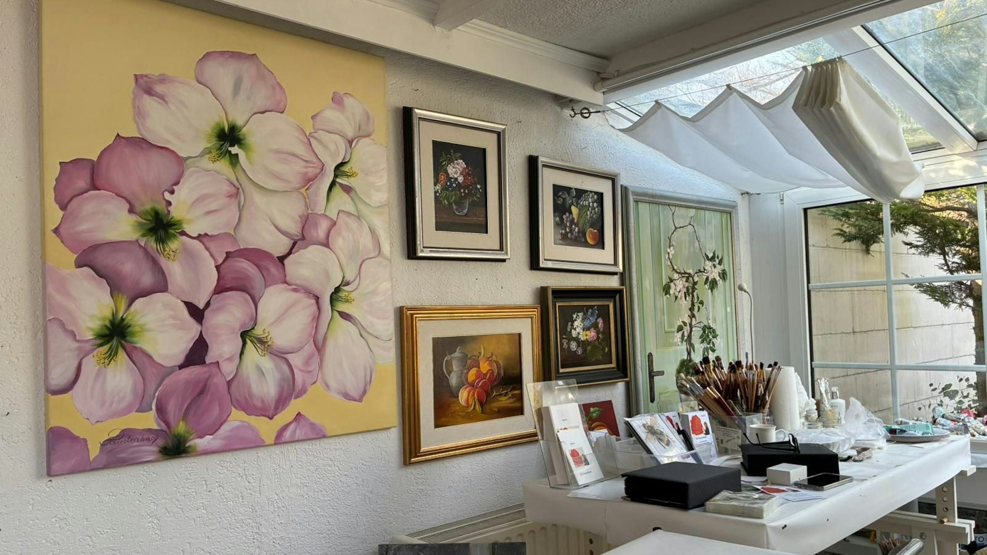 Im Atelier hängen viele Bilder von Blumen, auf einem Tisch stehen Pinsel und Farben.