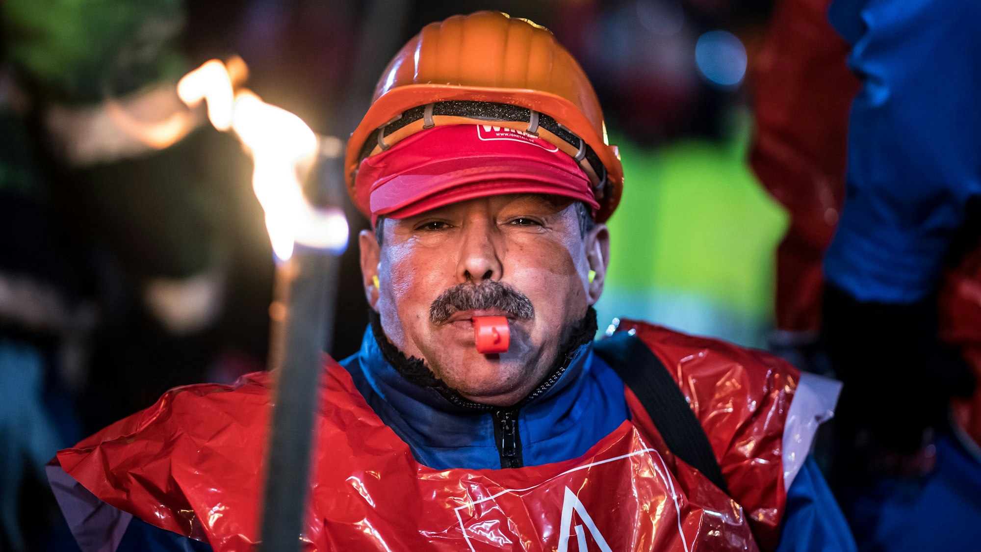 Ein Beschäftigter der Aluminium Norf GmbH in Neuss (Nordrhein-Westfalen) steht am 09.01.2018 bei einer Warnstreikversammlung der IG Metall mit einer brennenden Fackel und einer Trillerpfeife vor dem Werksgelände.