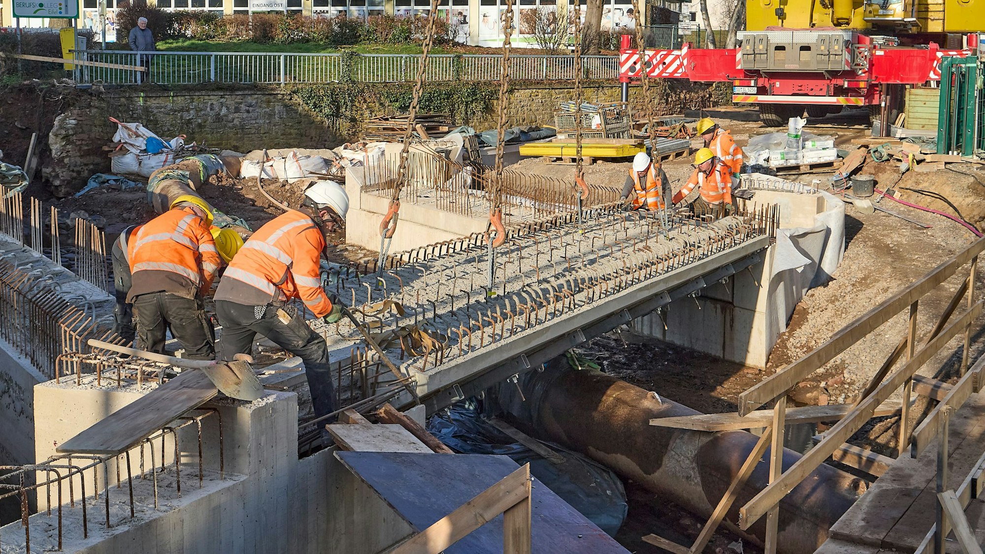 Fünf Männer tragen Warnjacken und Baustellenhelme. Sie bringen ein Bauteil einer Brücke in die exakte Position.
