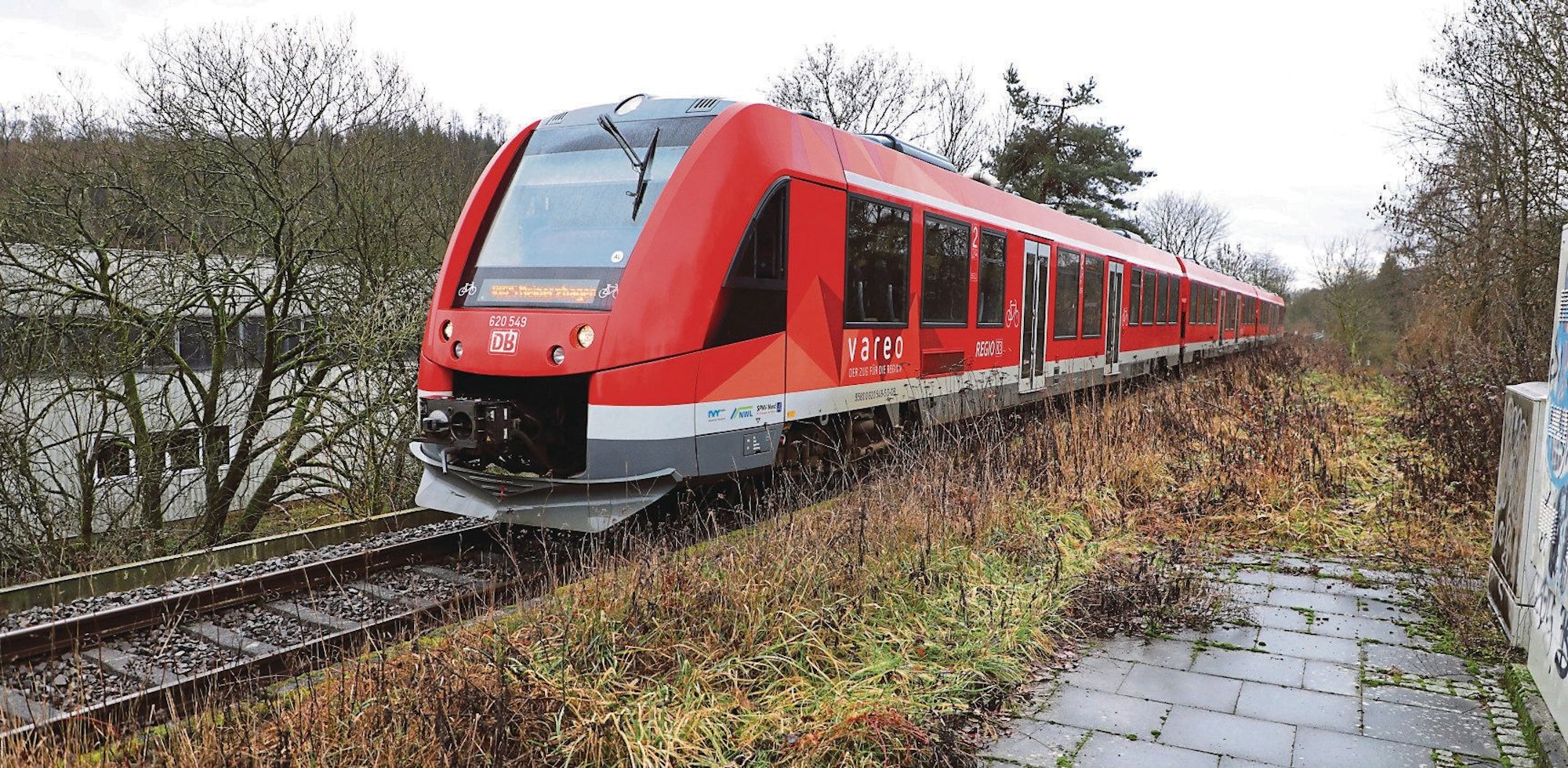 Eine Regionalbahn der RB 25 fährt auf der Regionalbahnstrecke in Overath-Vilkerath an einem gepflasterten Bereich vorbei.