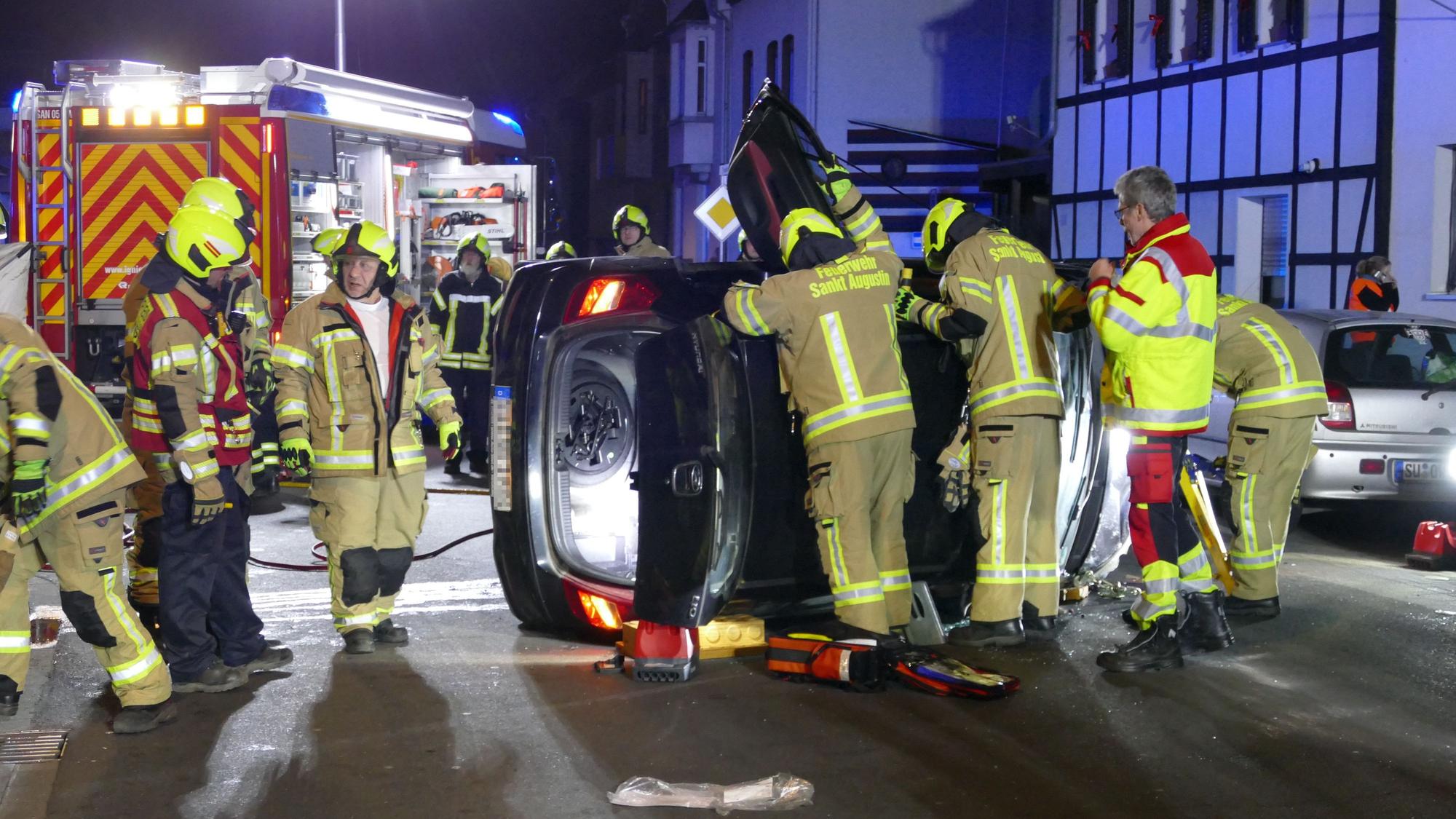 Feuerwehrleute in Sankt Augustin stehen an einem Fahrzeug, das auf der Seite liegt.