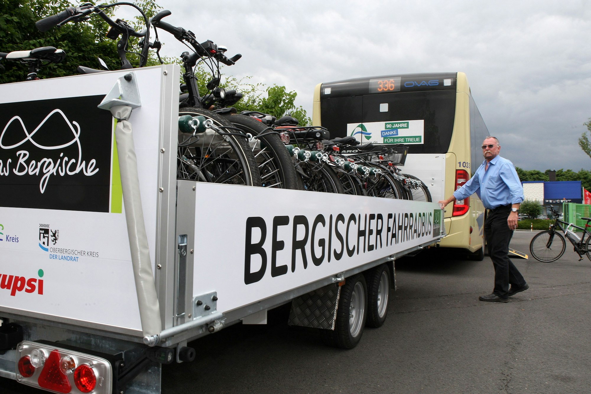 Ein Linienbus mit Fahrradanhänger, der Fahrer schließt die Seitenklappe.