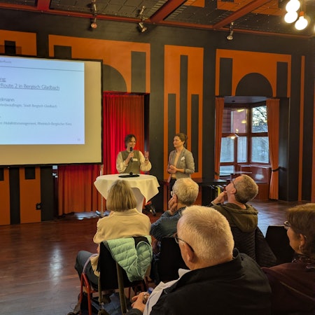 Das Foto zeigt den Gladbacher Spiegelsaal. Zwei Mitarbeitende der Verwaltung erklären den Verlauf der Radpendlerroute