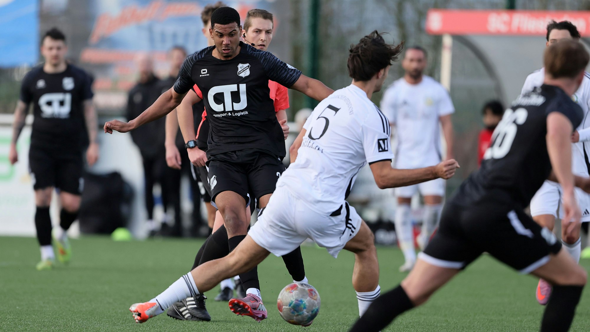 Dasd Foto zeigt einen Fußballer im scharzen Trikot, der den Ball an seinem Glescher Gegenspieler vorbei spitzelt.