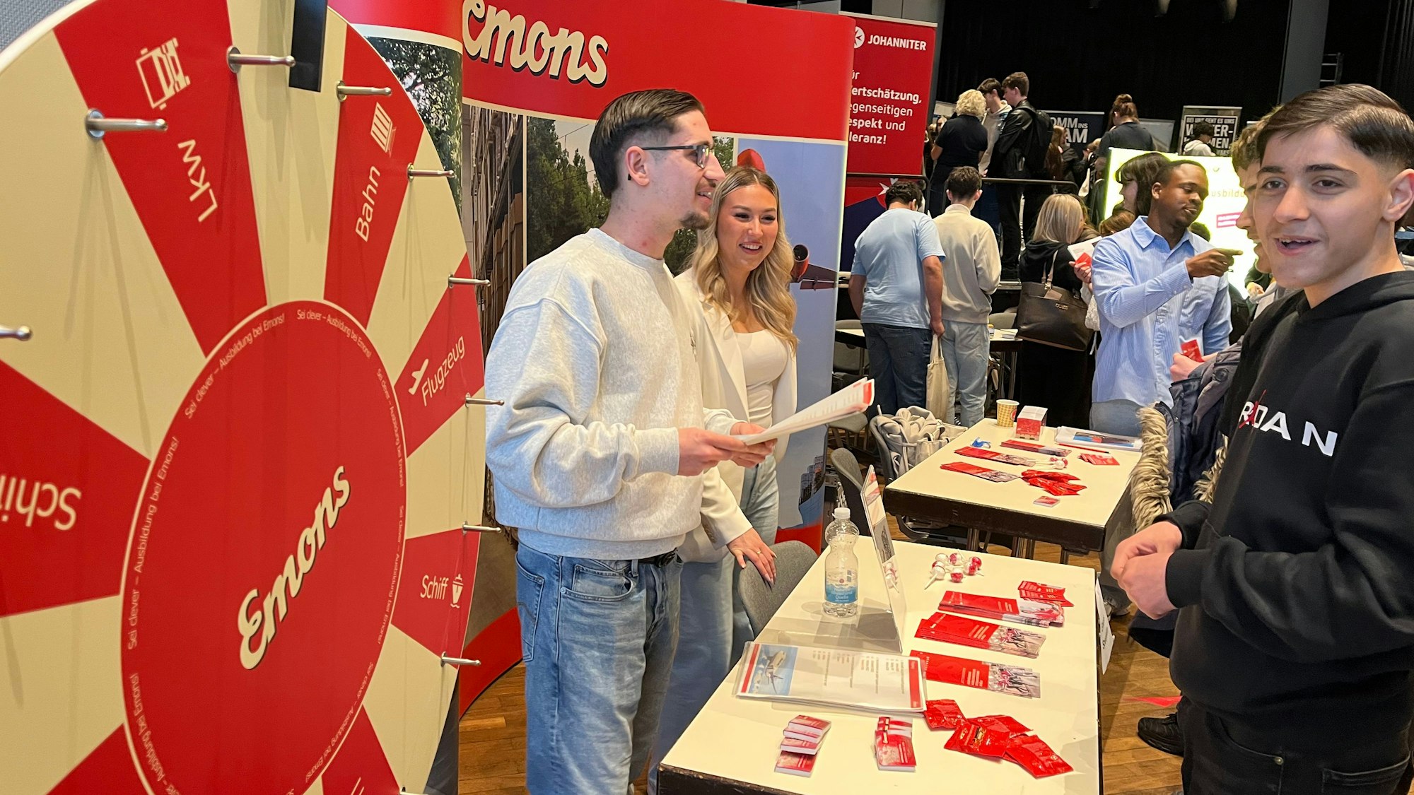 An einem Stand steht ein großes Glücksrad, viele junge Leute stehen davor.