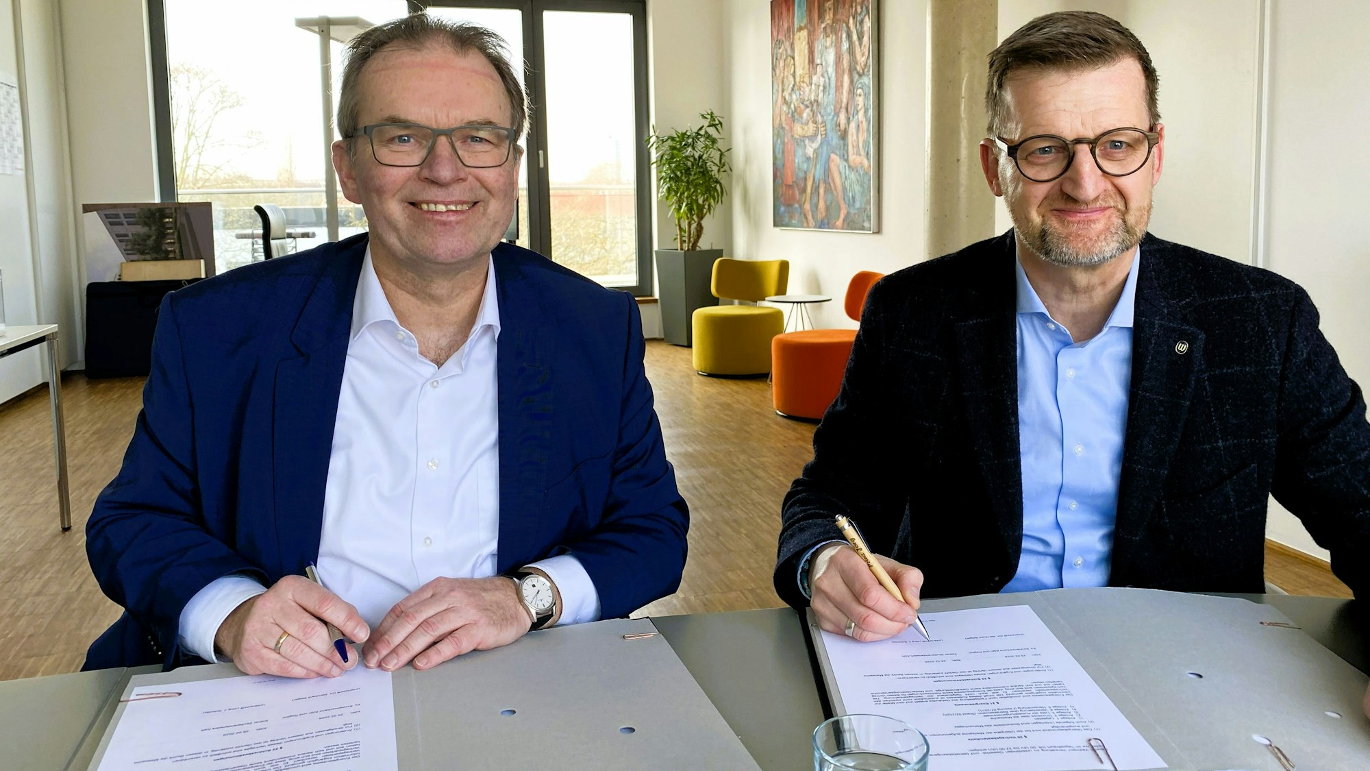 Zwei Männer sitzen an einem Tisch und unterzeichnen Schriftstücke