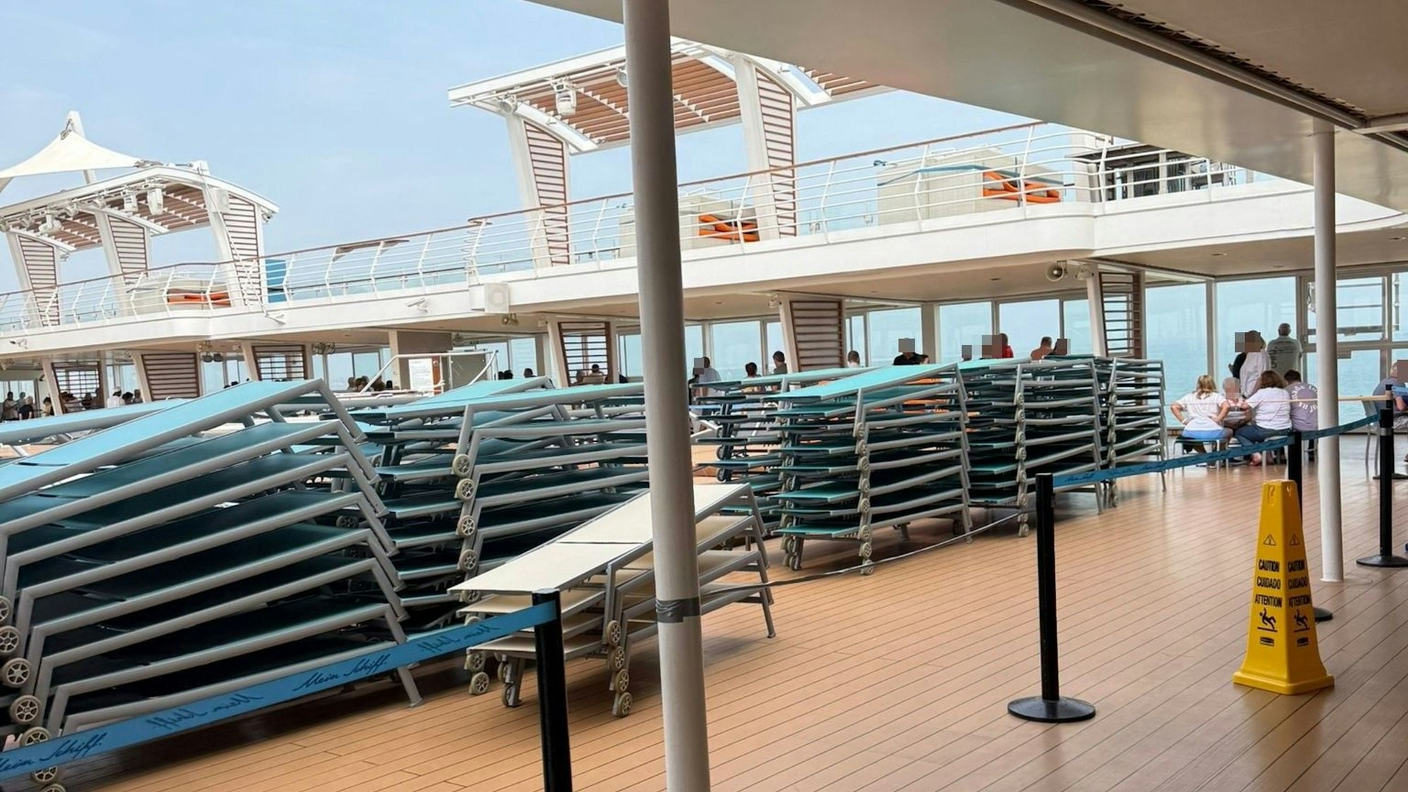 Auf dem Deck eines Kreuzfahrtschiffes sind zahlreiche Sonnenliegen aufeinandergestapelt.