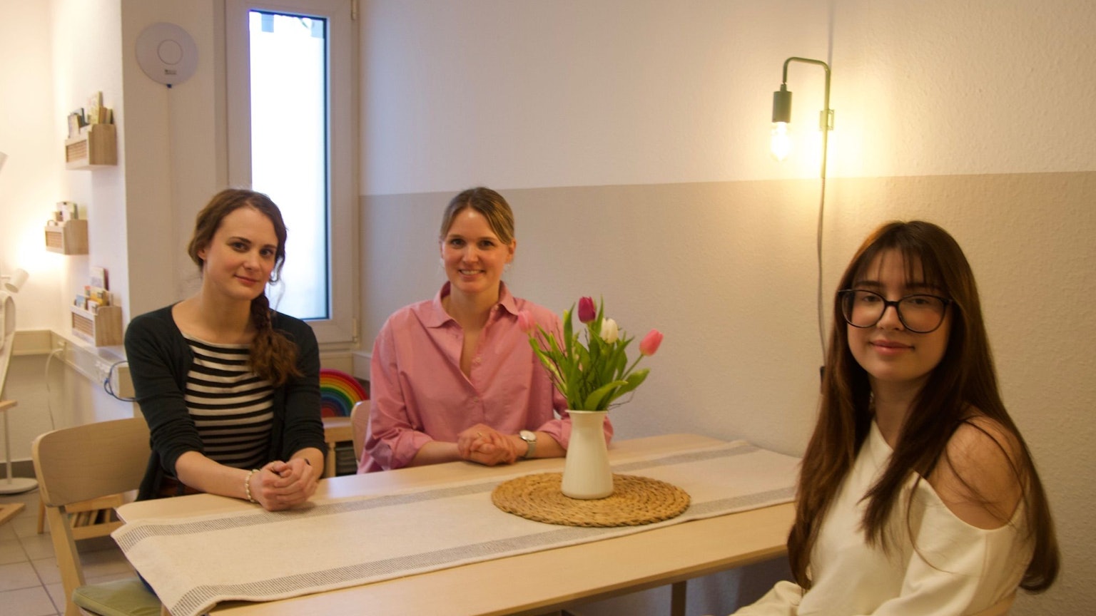 Drei Frauen sitzen an einem Tisch mit einem Strauß Blumen.
