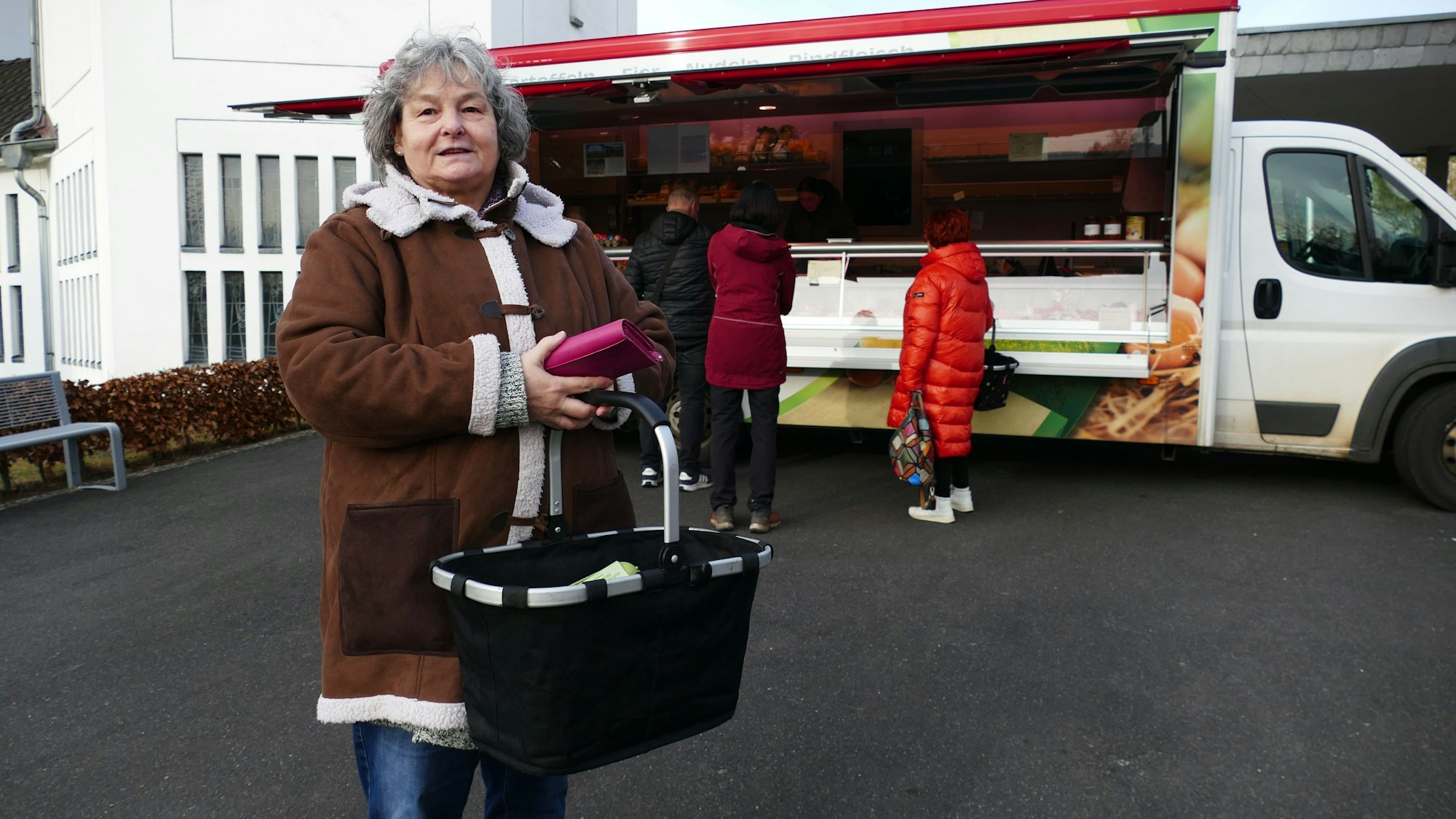 Petra Bonatz steht vor einem Stand und blickt in die Kamera. In der Hand hält sie einen Einkaufskorb und ihr Portmonee.
