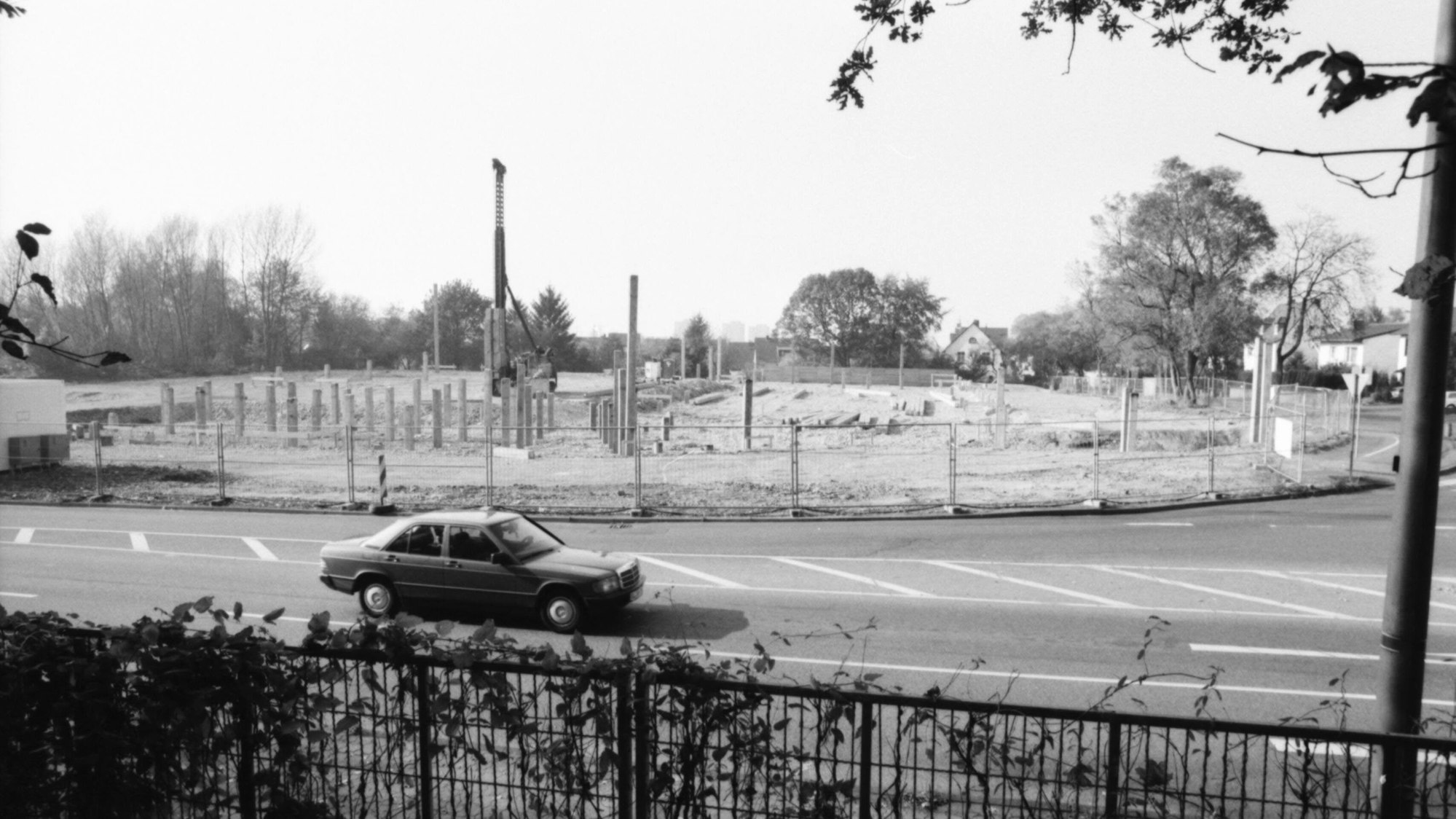 Man sieht ein altes schwarz-weiß Bild mit einem vorbeifahrenden Auto vor einer Baustelle.