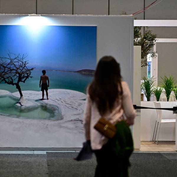 Eine Frau steht vor einem Urlaubfotoplakat mit Meer und Strand.