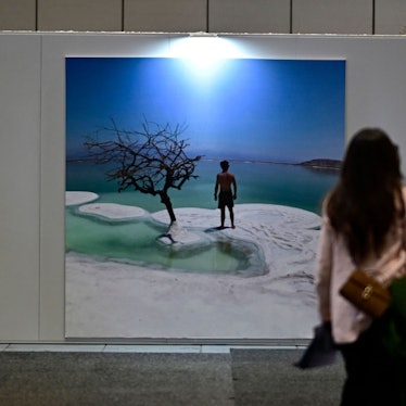 Eine Frau steht vor einem Urlaubfotoplakat mit Meer und Strand.