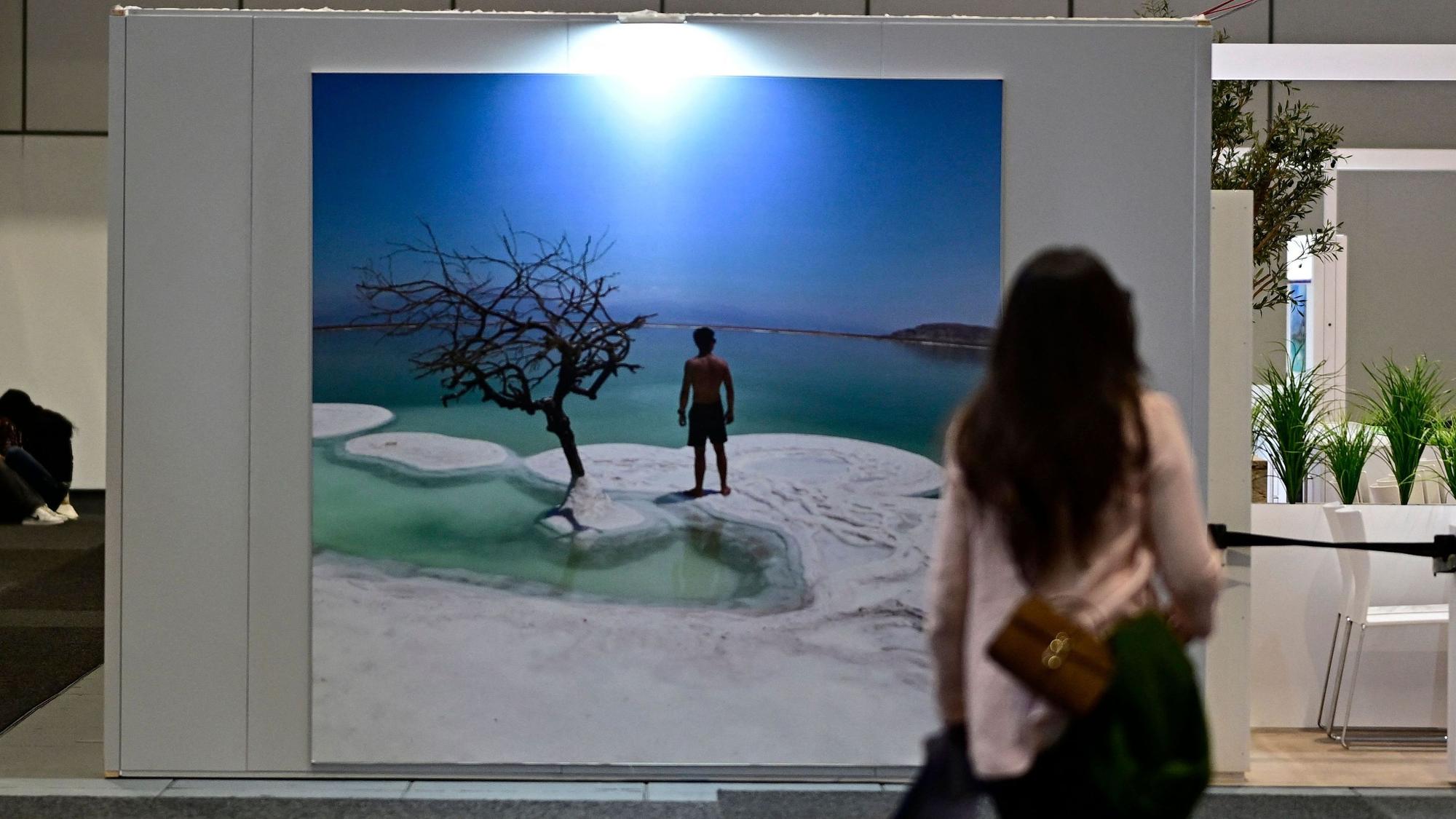 Eine Frau steht vor einem Urlaubfotoplakat mit Meer und Strand.
