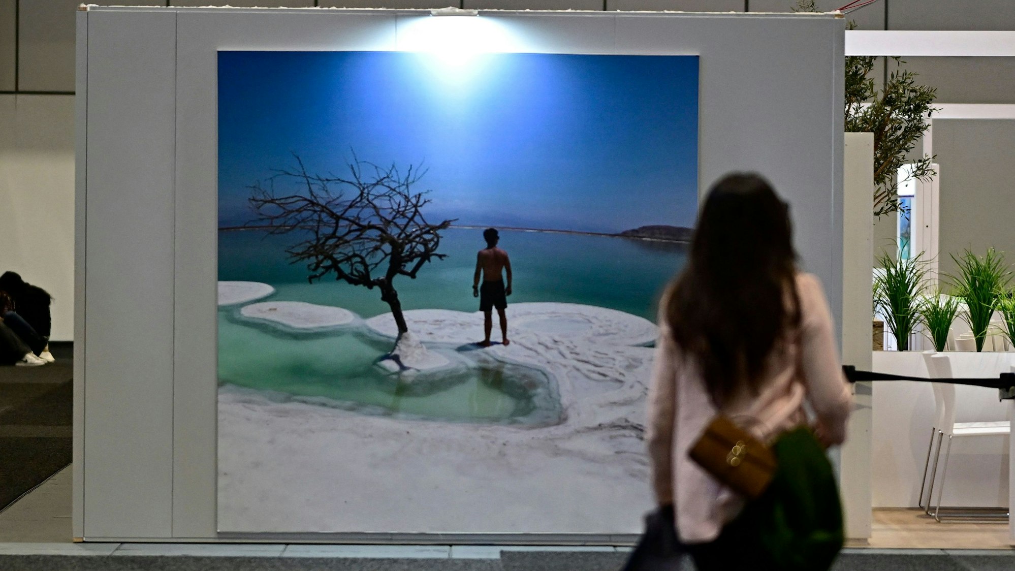 Eine Frau steht vor einem Urlaubfotoplakat mit Meer und Strand.