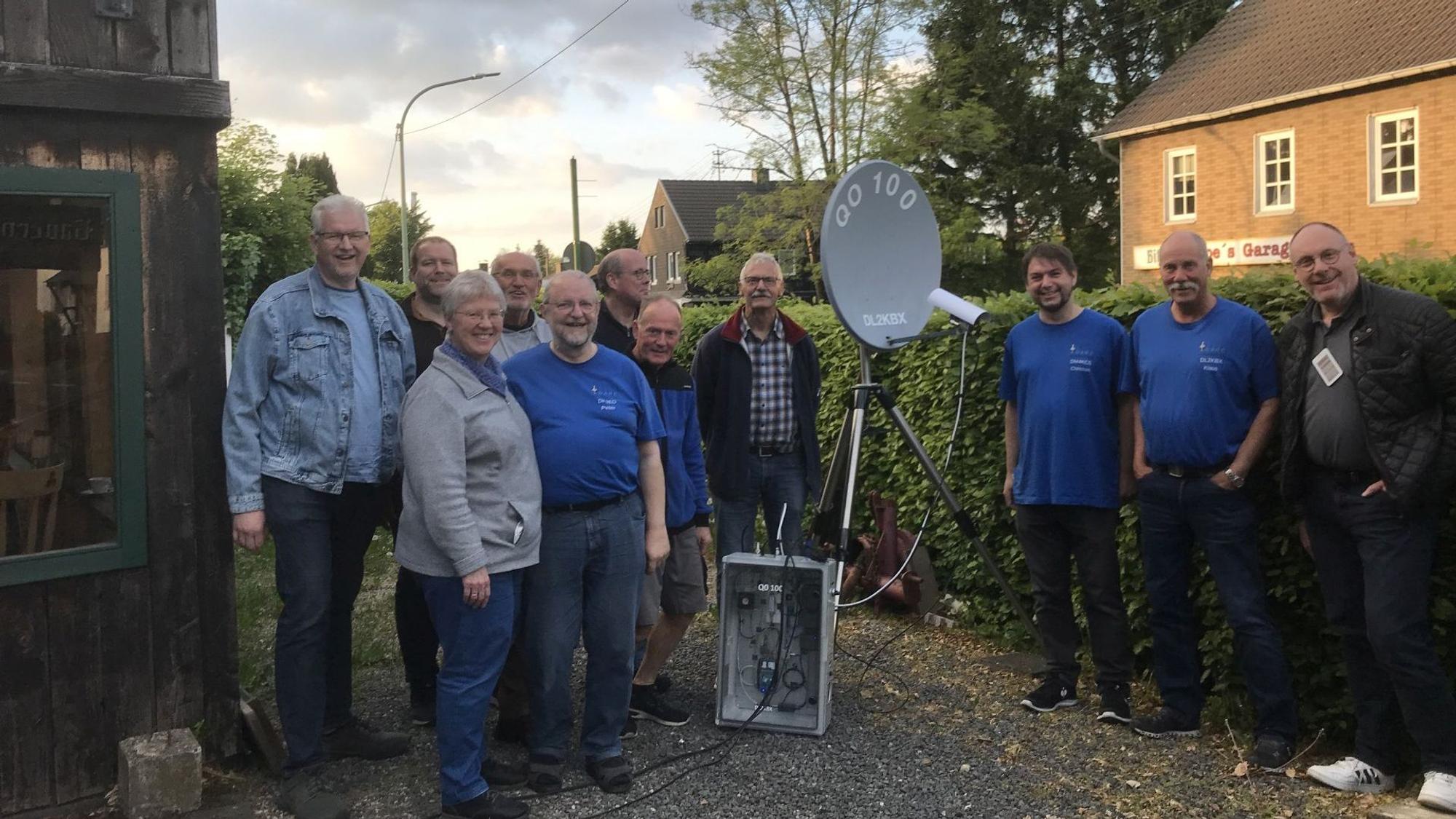 Zehn Männer und eine Frau stehen um eine mobile Satellitenschüssel herum.