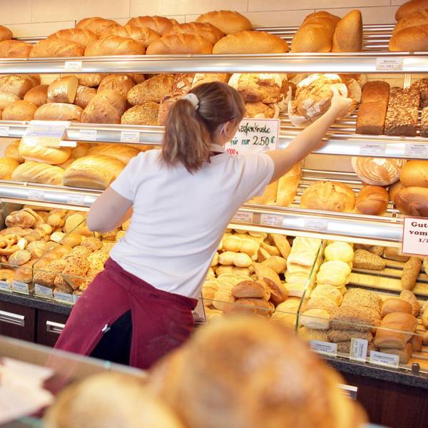 Eine Verkäuferin holt in einer Bäckerei ein Brot aus dem Regal.