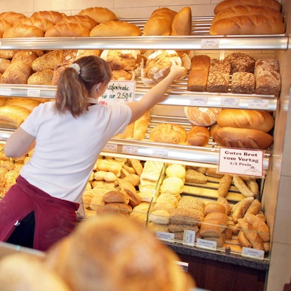 Eine Verkäuferin holt in einer Bäckerei ein Brot aus dem Regal.