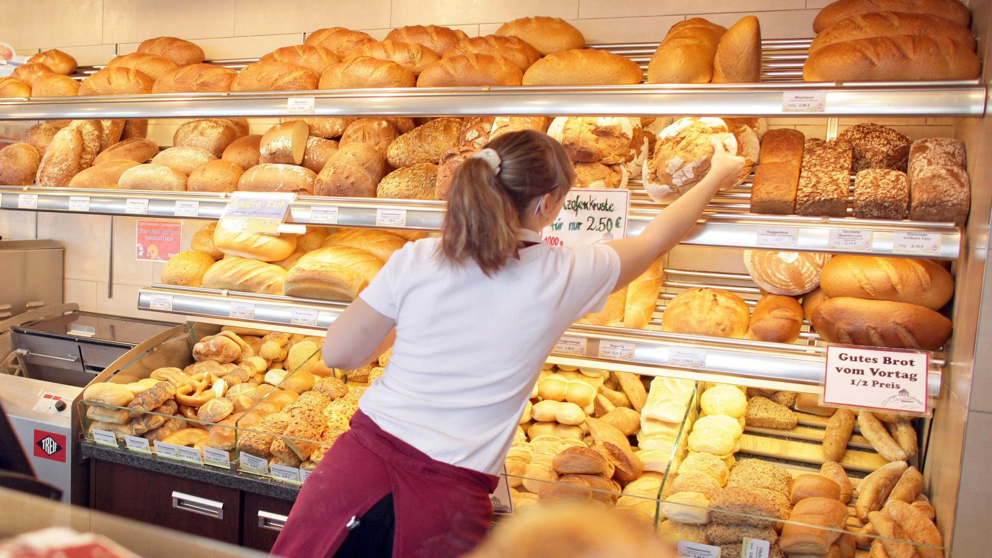 Eine Verkäuferin holt in einer Bäckerei ein Brot aus dem Regal.