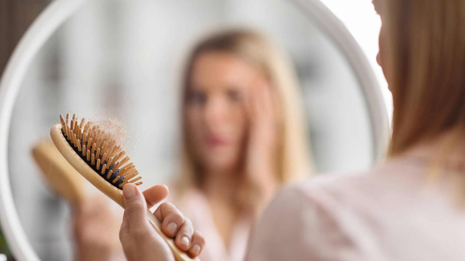 Eine Frau vor dem Spiegel betrachtet ihre Haarbürste.