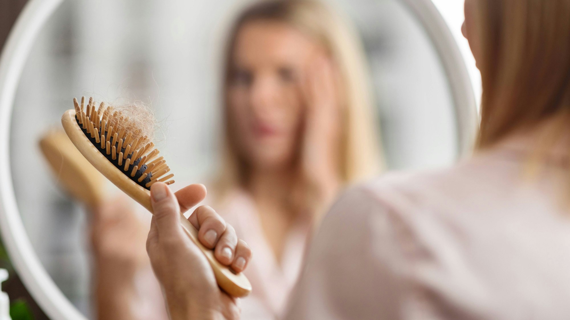 Eine Frau vor dem Spiegel betrachtet ihre Haarbürste.