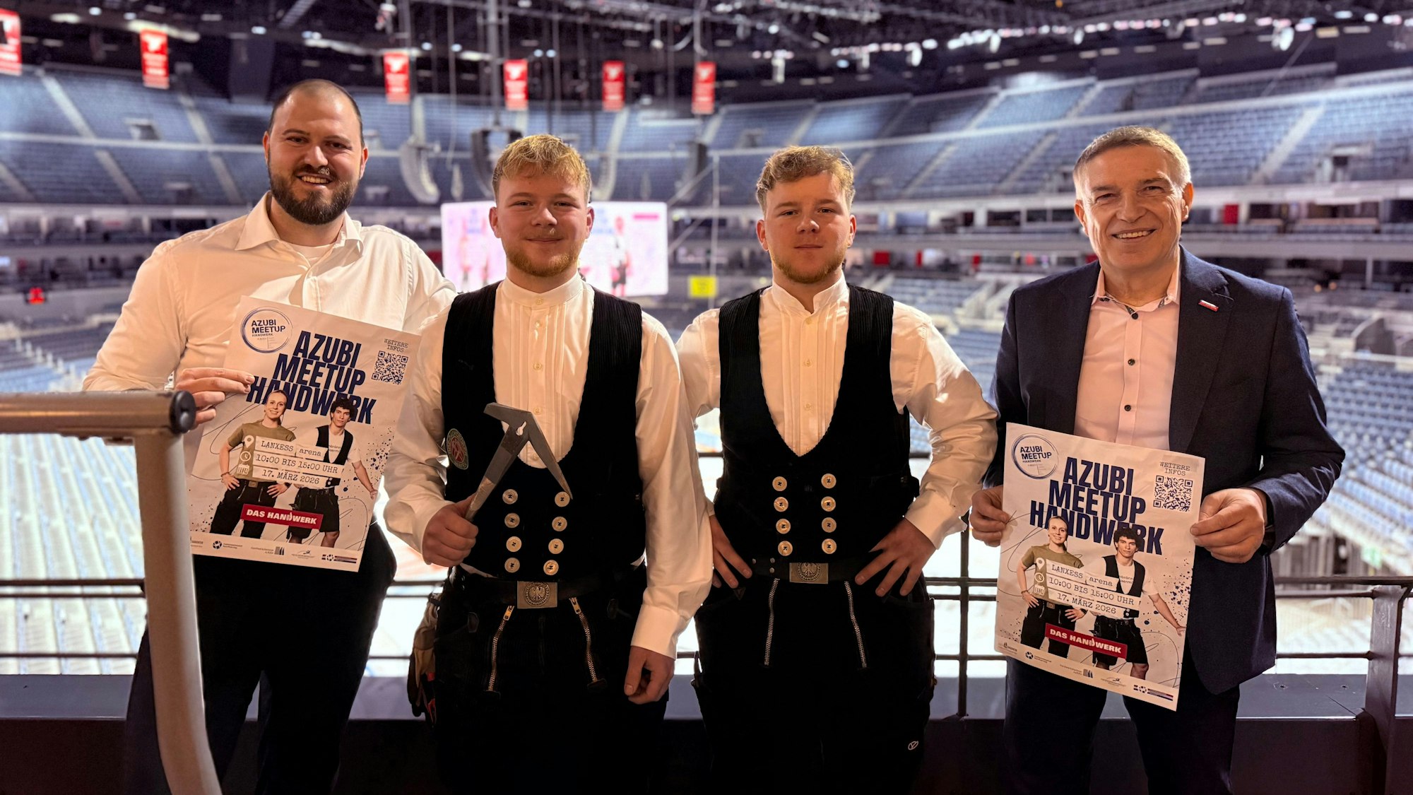 Carsten Heling von der Lanxess-Arena, Noah und Noel Mohr sowie HWK-Geschäftsführer Erik Werdel stehen auf der Tribüne der Lanxess-Arena. Sie präsentieren Plakate der Ausbildungsmesse.