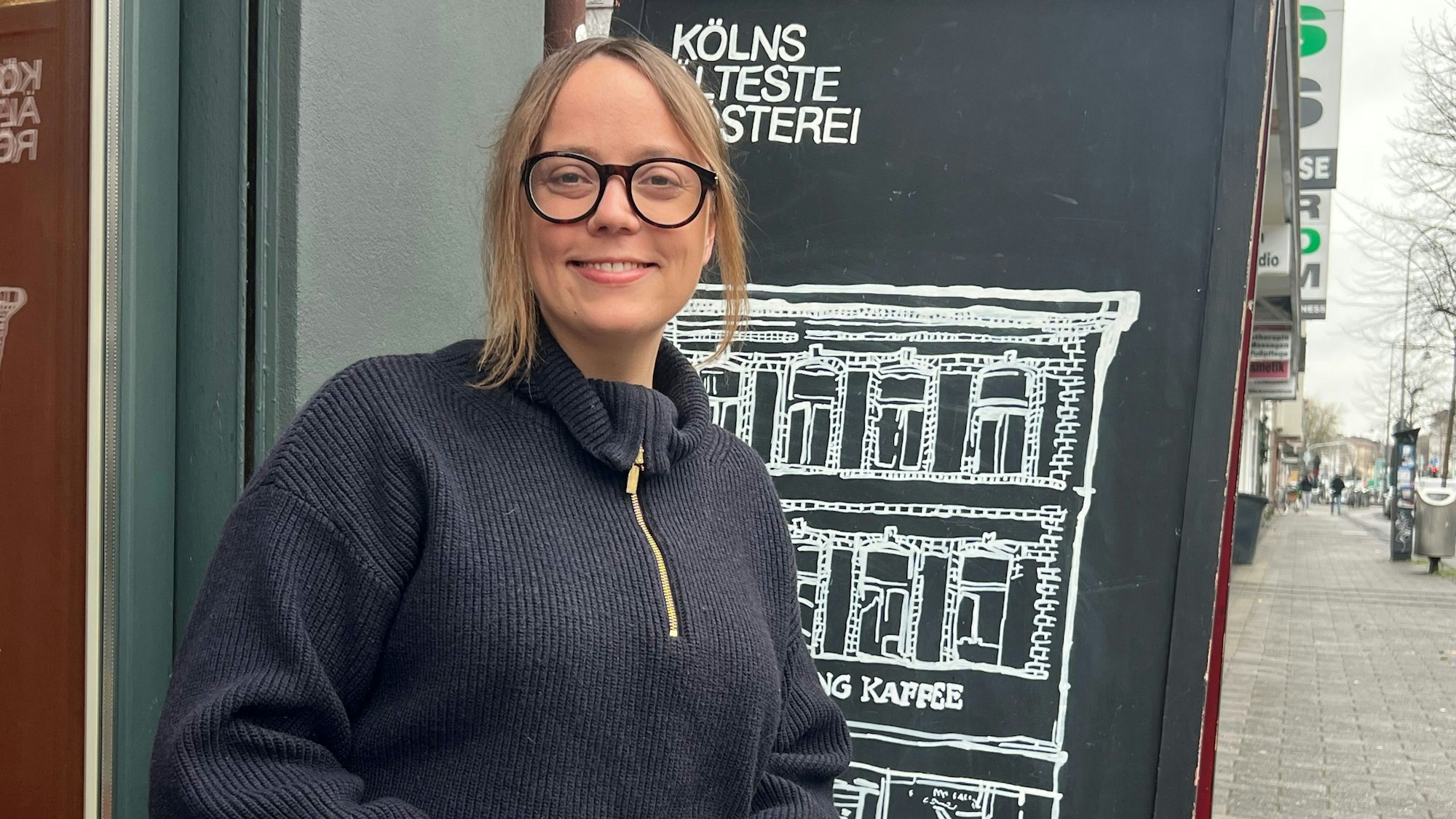 Evita Fernandez sitzt mit einem Kaffee vor einem Cafe.