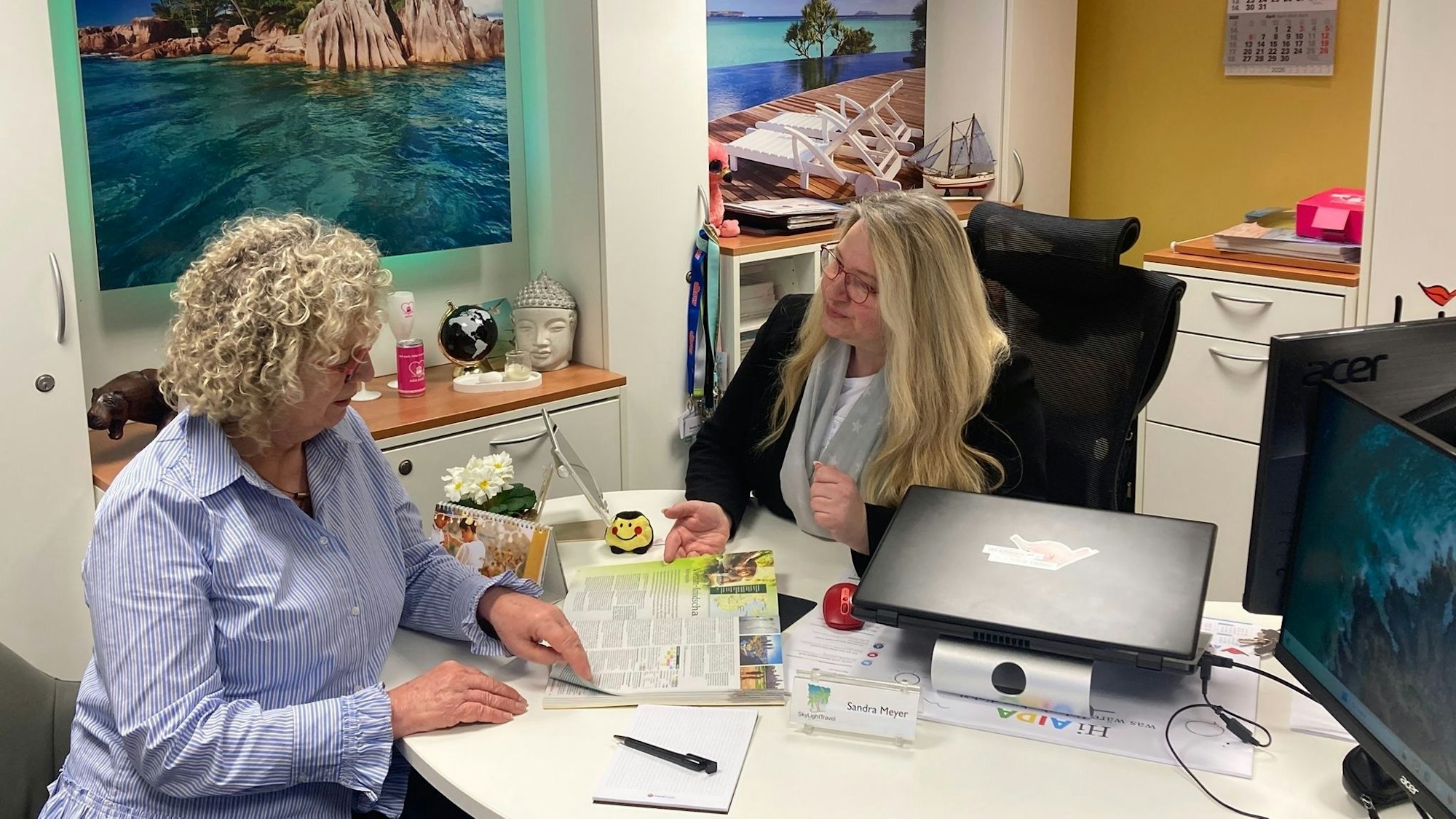 Zwei Frauen im Gespräch, eine blättert in einem Reiseprospekt.