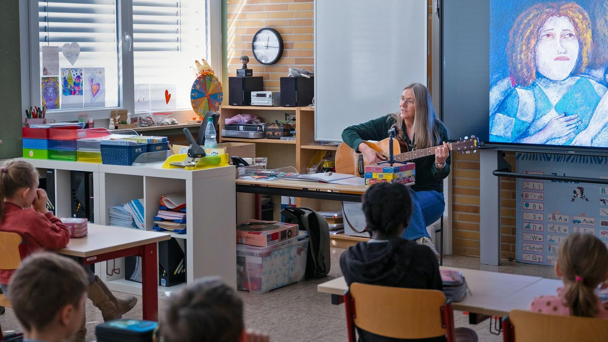 Ein Frau spielt Gitarre im Klassenzimmer.