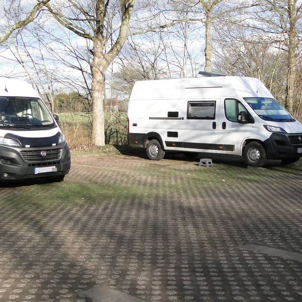 Drei Wohnmobile stehen auf einem großflächigen Parkplatz.