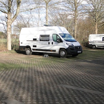 Drei Wohnmobile stehen auf einem großflächigen Parkplatz.