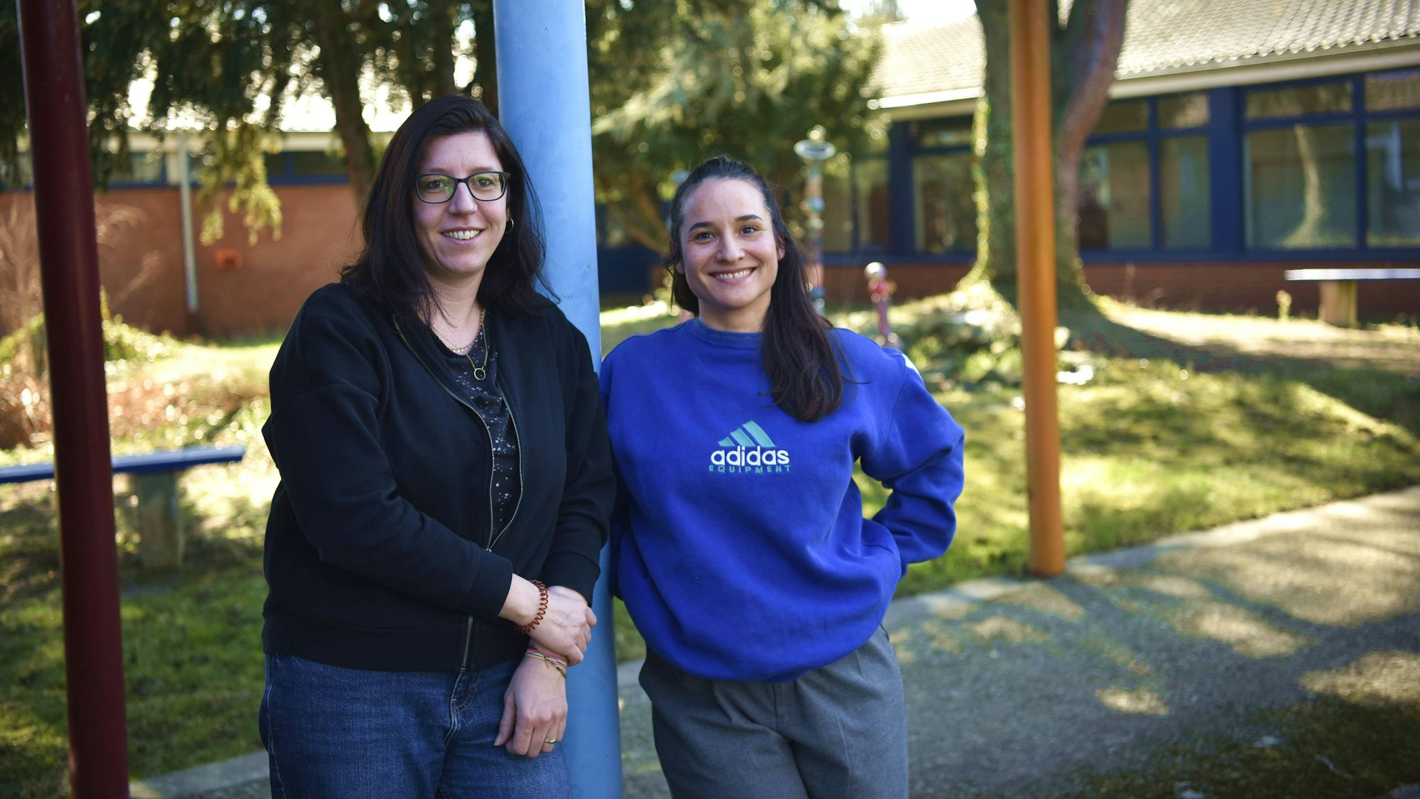 Nadine Cherubini (links) und Inga Hülshoff stehen an eine blaue Säule gelehnt auf dem Schulhof der Zülpicher Hauptschule.