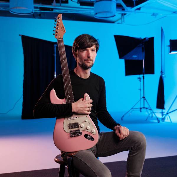 Philipp Brämswig hält seine Gitarre vor der Brust.