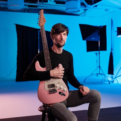 Philipp Brämswig hält seine Gitarre vor der Brust.