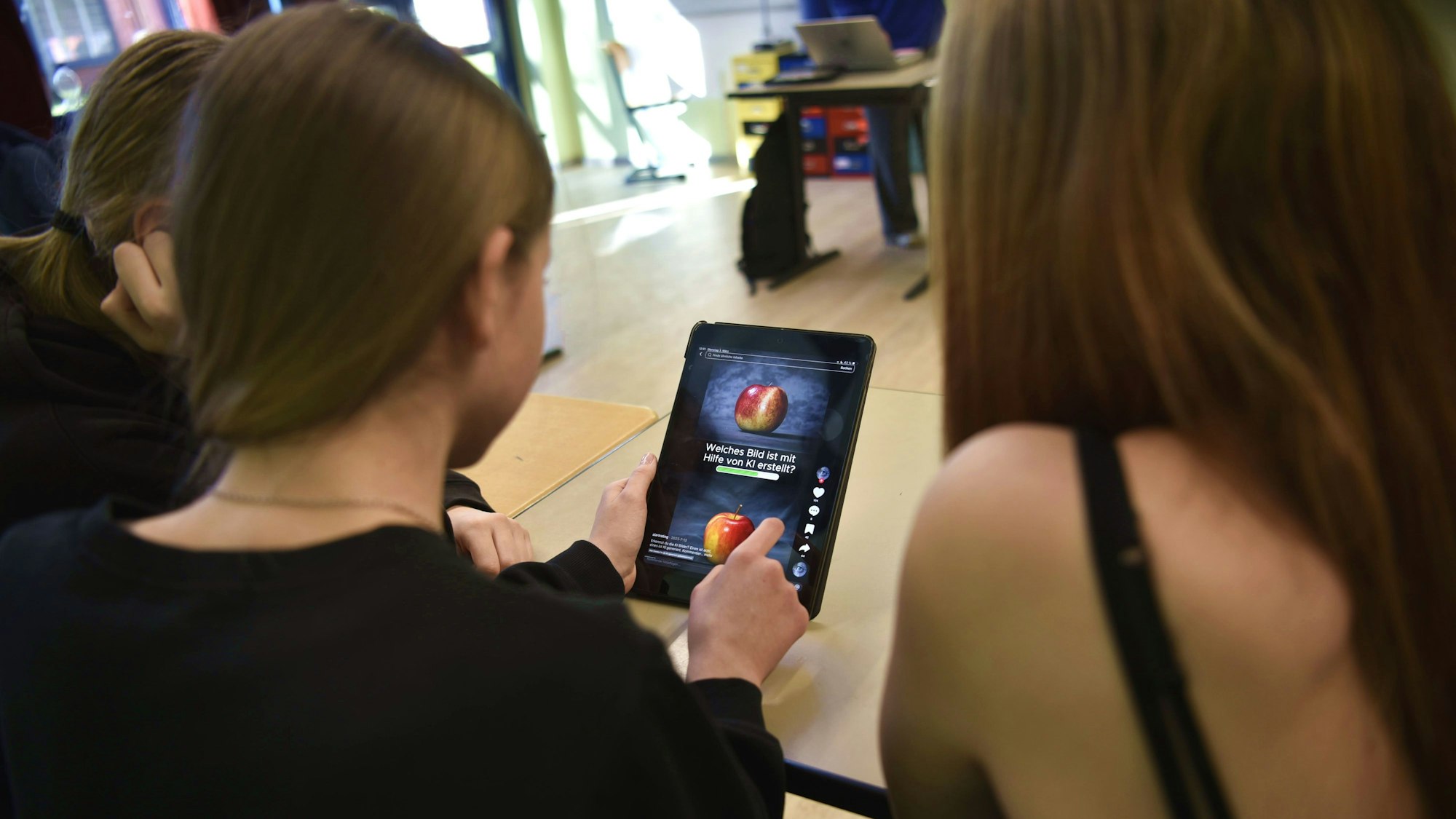 Schülerinnen der Jahrgangsstufe acht beugen sich über ein Tablet und scrollen durch TikTok.