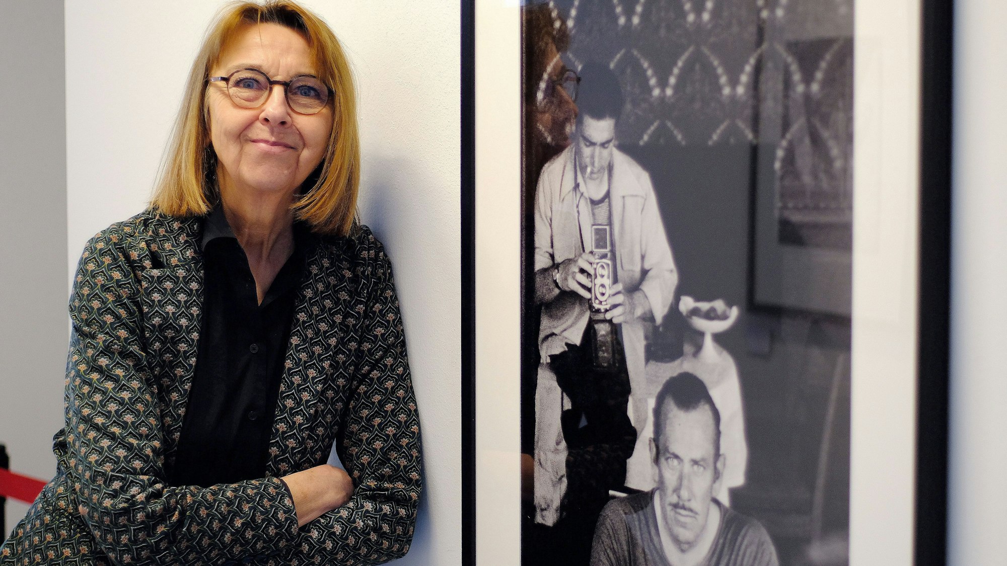 Dr. Nina Mika-Helfmeier, Leiterin und Kuratorin des Fotografie-Forums der Städteregion Aachen in Monschau, steht neben einem Foto, das Robert Capa und John Stinbeck zeigt.