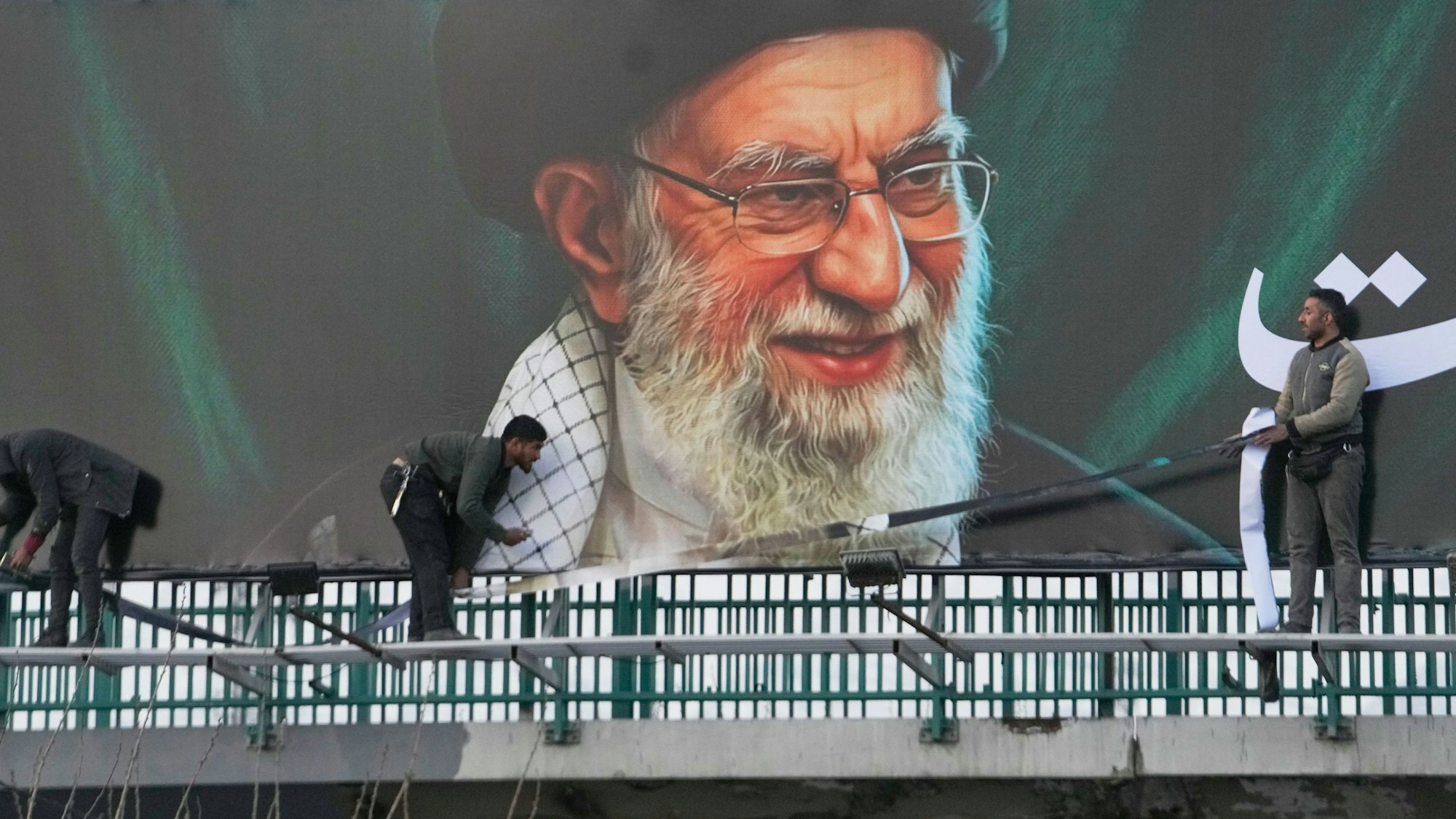 Arbeiter montieren eine Plakatwand mit dem Porträt des verstorbenen iranischen Obersten Führers Chamenei.