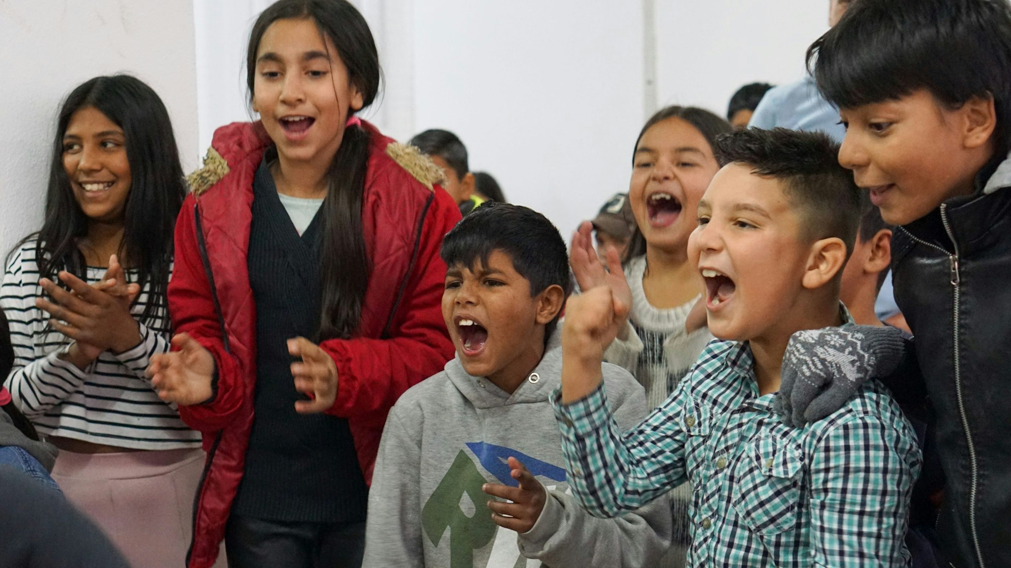Zahlreiche Kinder stehen nebeneinander. Einige klatschen und schreien.