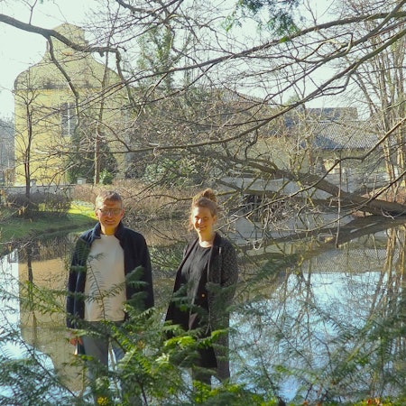 Dorothee Lindenbaum und Stefan Bergner (l.) stehen am Wassgeraben, in dem sich die Burg Flamersheim spiegelt.