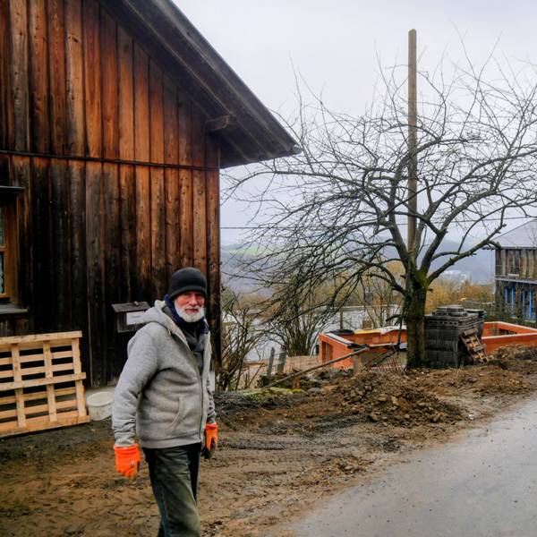 Ein Mann steht mit Mütze und Handschuhen auf der Straße. Im Hintergrund sind die Häuser, dass eine noch im Rohbau, zu sehen.