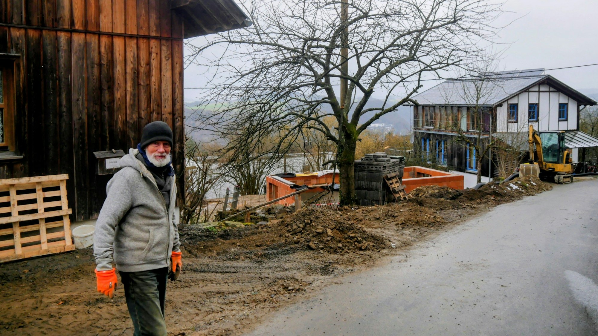 Ein Mann steht mit Mütze und Handschuhen auf der Straße. Im Hintergrund sind die Häuser, dass eine noch im Rohbau, zu sehen.