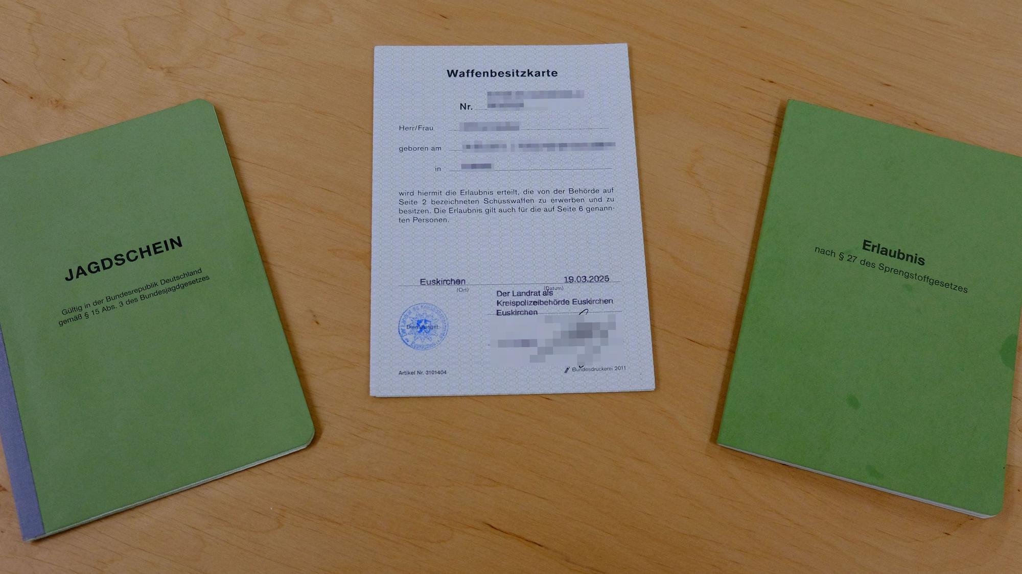 Jagdschein, Waffenbesitzkarte und Sprengstoffschein liegen nebeneinander auf einem Holztisch.