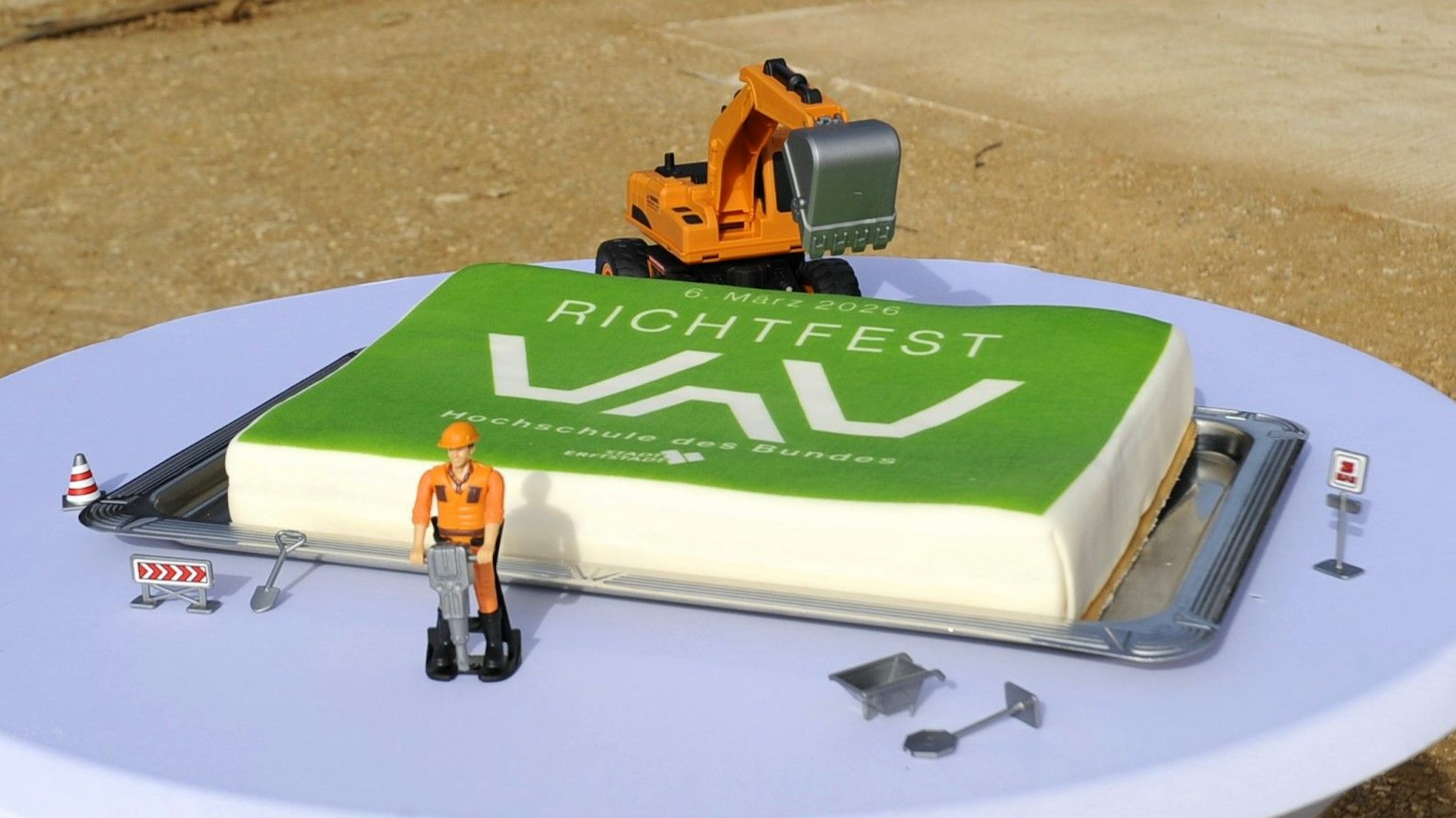 Zu sehen ist eine Torte mit grünem Fondant und einem Spielzeugbagger und weiteren Baustellenspielzeugen.