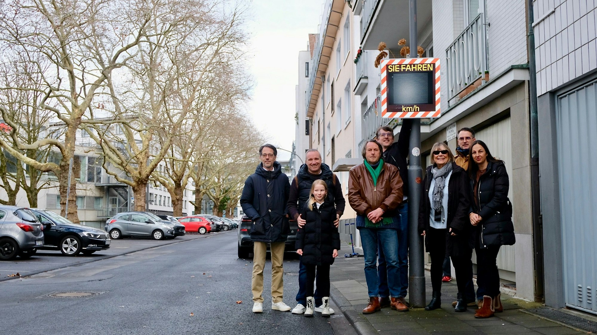 Eine Gruppe Menschen steht um einen Geschwindigkeitsmessmast herum.
