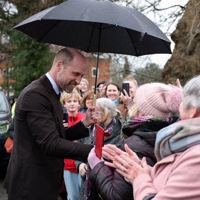 Prinz William unter Regenschirm mit lächelnden Menschen