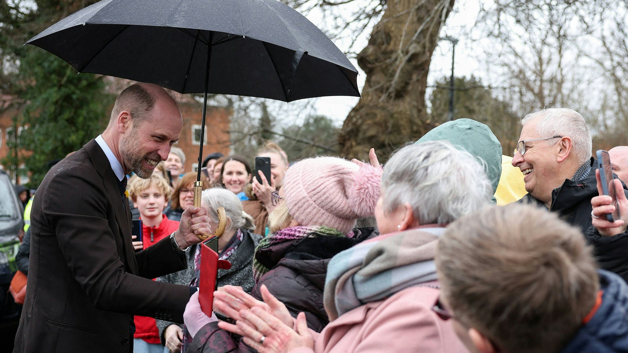 Prinz William unter Regenschirm mit lächelnden Menschen