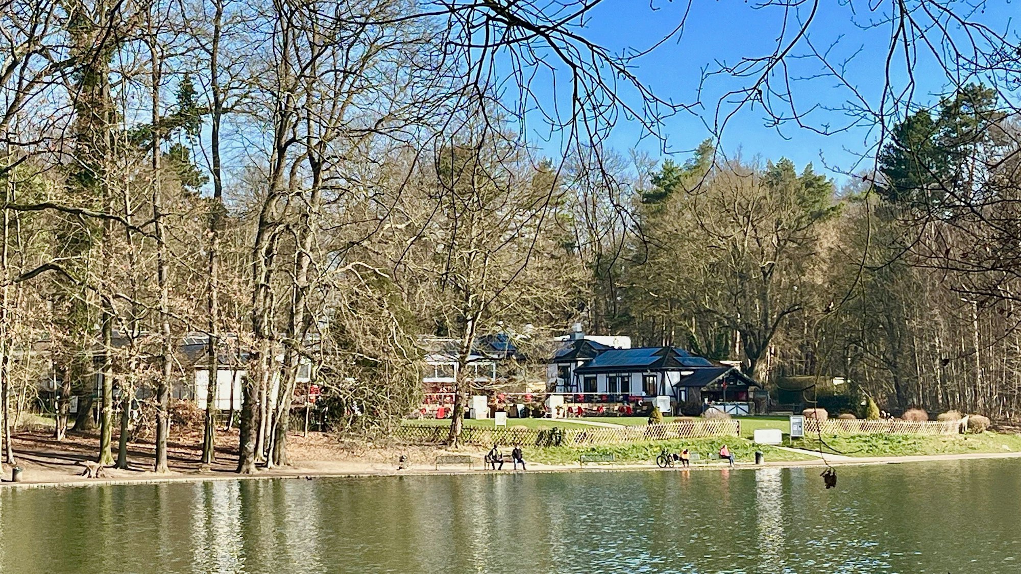 An einem See liegt ein großes Gebäude mit Rasenfläche davor.