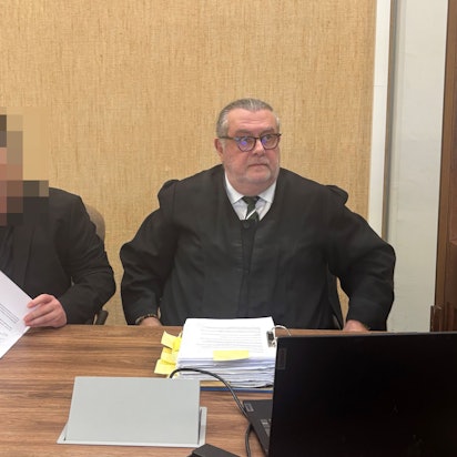 Der Angeklagte sitzt im schwarzen Anzug mit roter Krawatte neben seinem Verteidiger Thomas Düber.