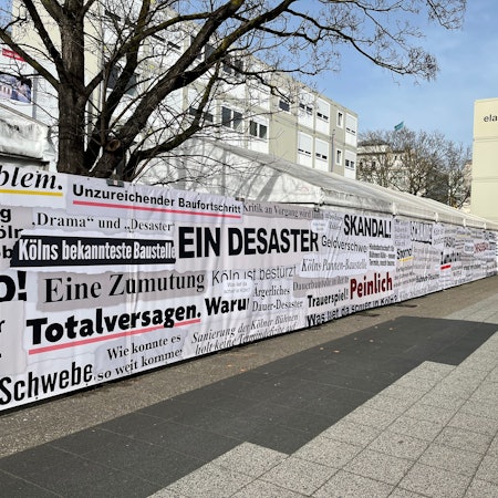 „Totalversagen“ oder „Desaster“: Der sogenannte „Frustzaun“ an der Bühnen-Baustelle am Offenbachplatz zeigt Schlagzeilen der vergangenen 14 Jahre.