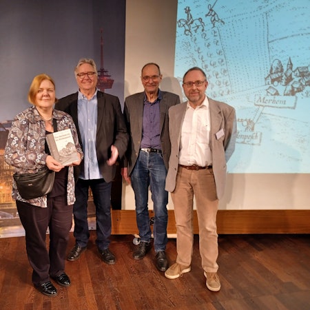 Eine Frau und drei Männer stehen vor einer Leinwand.