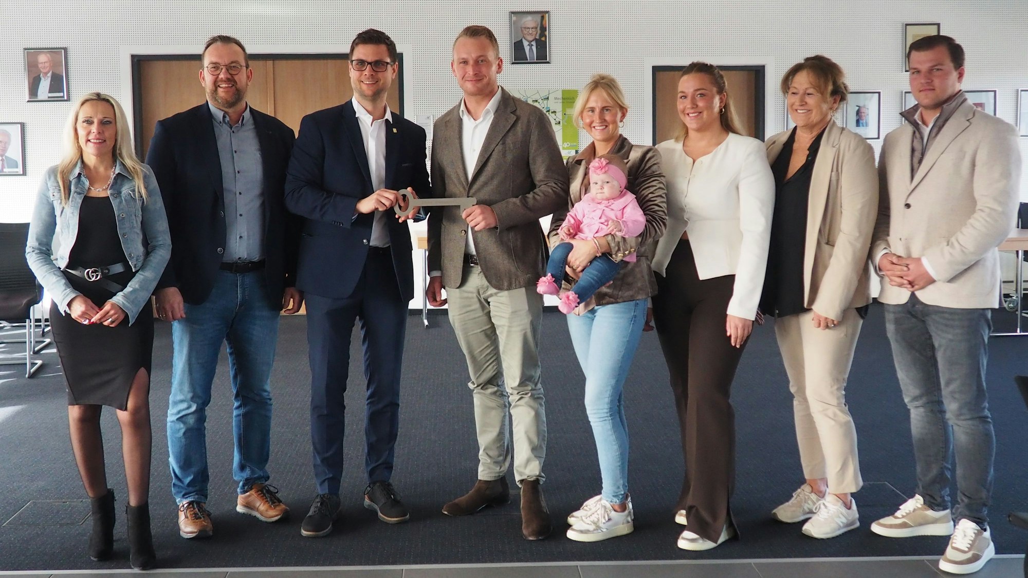 Acht Männer und Frauen stehen in einer Reihe. Bürgermeister Fingel übergibt Roland Barth einen großen Schlüssel. Eine Frau hält ein Baby im Arm.